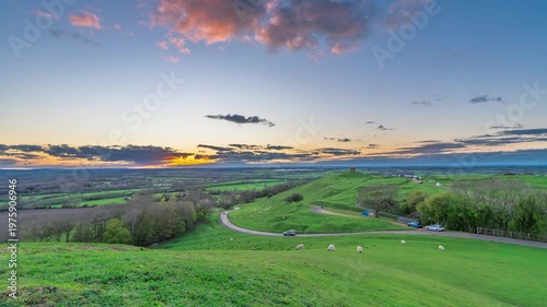 Sunset over rolling green hills with grazing sheep