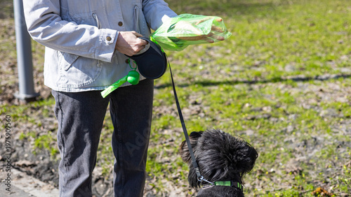 Fotografie Woman using poop bag dispenser outdoors, responsible pet care, hygiene practice, urban service, cleanliness