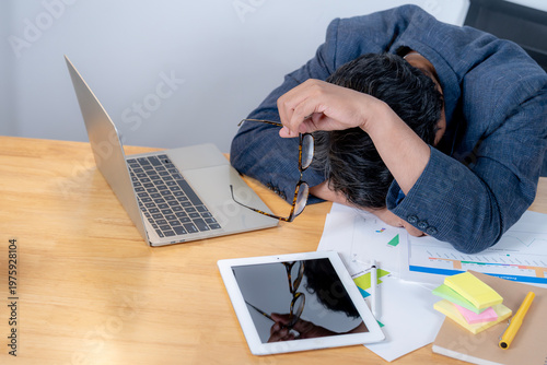 Tired young male employee looking exhausted while sitting at his desk after working for a long period.