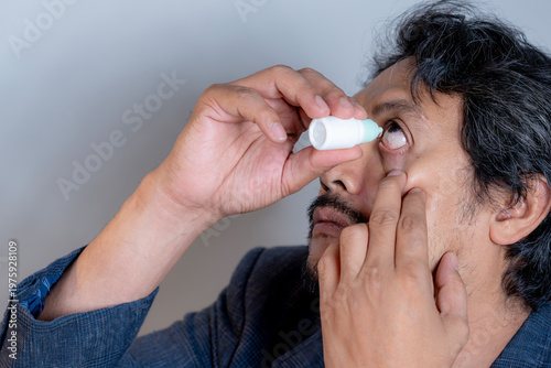 Male professional applying eye drops at his desk to relieve dry eye symptoms caused by long hours of computer screen exposure.