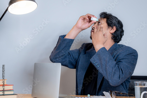 Male professional applying eye drops at his desk to relieve dry eye symptoms caused by long hours of computer screen exposure.