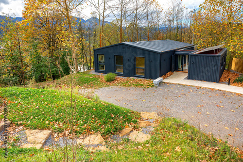 Autumn trees and blue sky landscape with modern house built from repurposed shipping containers, showcasing modular, sustainable architecture as part of eco friendly workspace design