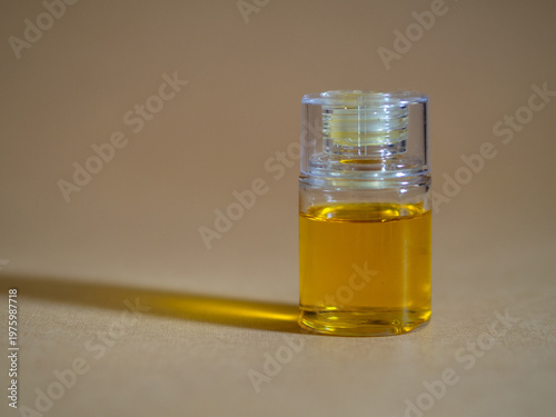 Minimalist close-up of a small transparent glass bottle filled with golden liquid oil, isolated on a neutral beige background