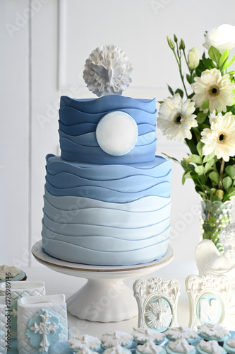 elegant religious celebration cake table with blue and white decor, modern baptism or first communion event setup with floral arrangements and angel souvenirs, spiritual ceremony decoration