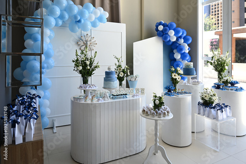 elegant blue and white party decoration with balloons and cylindrical pedestals, modern birthday or baby shower setup with floral arrangements and sweets, minimalist event decor in a bright room
