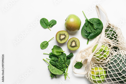 Fresh green vegetables and fruits in reusable mesh bag on white background with apple, spinach, broccoli, avocado and kiwi 