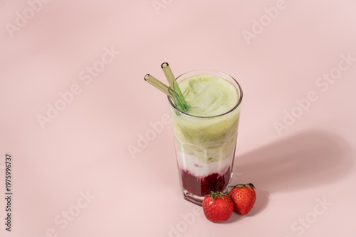 Strawberry matcha latte in clear glass on pastel light pink background with copy space, layered iced drink, minimal aesthetic
