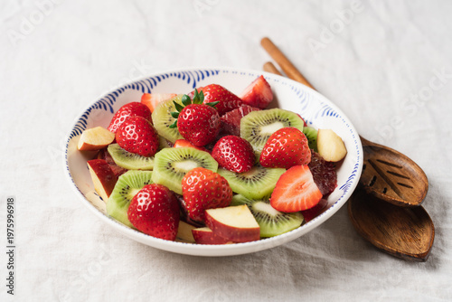Fresh summer fruit salad with strawberries and kiwi in ceramic bowl on table with linen tablecloth, healthy seasonal dessert concept