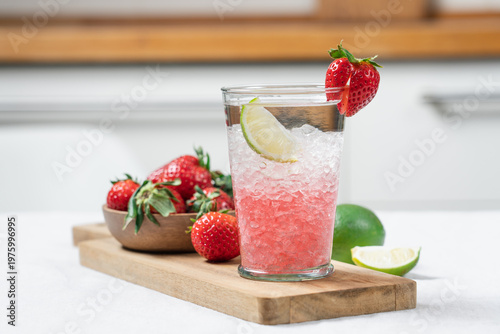 Refreshing strawberry summer drink with ice and lime in glass on light kitchen background, homemade cold beverage concept