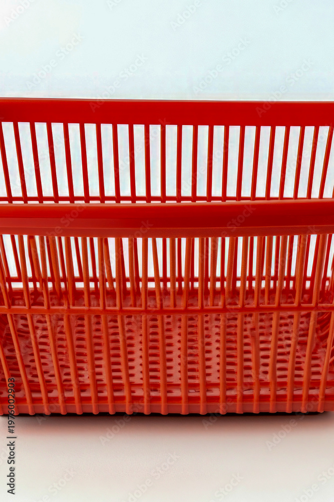 Fototapeta premium A small, bright red plastic basket sits on a clean white surface. vertical frame