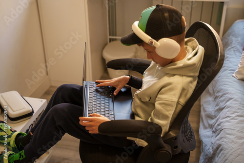 Slika na platnu Niño concentrado usando un ordenador portátil con auriculares en su habitación