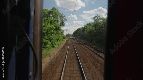 Point of view from the back of a moving train. Railway tracks receding into the distance as the train travels through the countryside