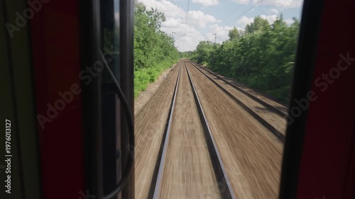 Rear point of view from a fast-moving train. Railway tracks recede into the distance as the train travels through a green landscape