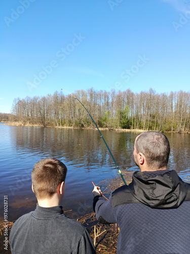 A father and son fishing. The father explains how to cast the rod.