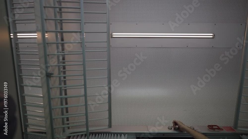 Male technician's hand is pressing a button to turn on a long fluorescent tube light attached to a perforated wall in a modern workshop