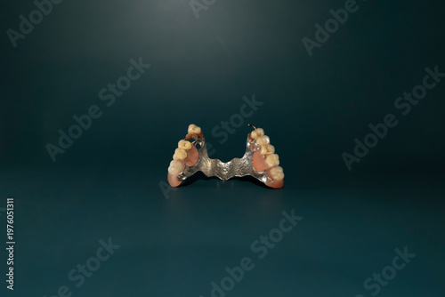 Removable partial denture with artificial teeth and metal base on dark green background. Studio macro photography isolated object. Dentistry and oral healthcare concept. Design for poster, banner.