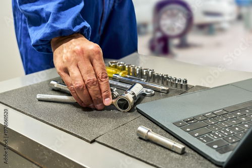 Foto Repairman's hands grabbing a tool from his toolbox and consulting his laptop for information about the car