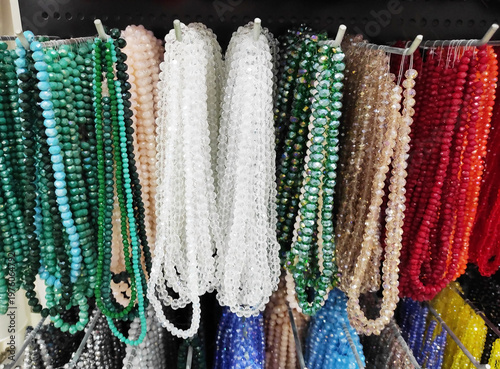 Colorful strands of beads hanging on display, variety of vibrant glass beads for jewelry making, craft supplies in different colors, textured background with rich assortment