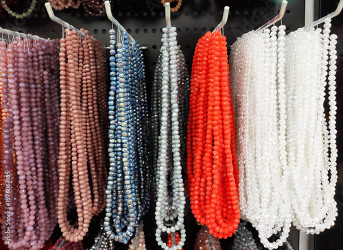 Colorful strands of beads hanging on display, variety of vibrant glass beads for jewelry making, craft supplies in different colors, textured background with rich assortment
