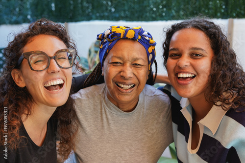 Portrait of multi generational women smiling on camera outdoor - African mother and daughter with caucasian girlfriend - Lifestyle, multiracial people and friendship concept