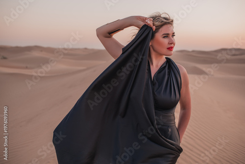 Close up portrait of elegant blond woman in black dress in desert, UAE. 
