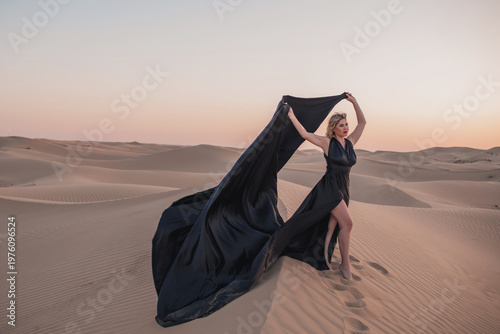 Luxury fashion woman posing in sand dunes with flowing black dress.