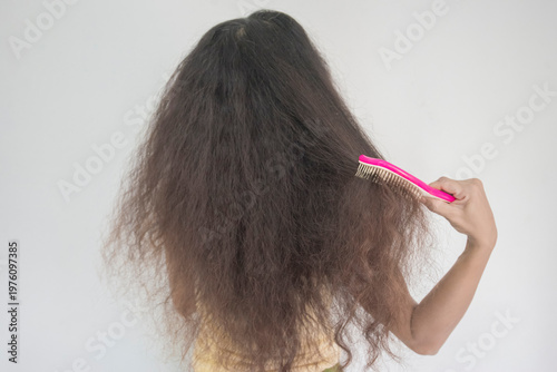 A young woman with curly hair is combing her hair.