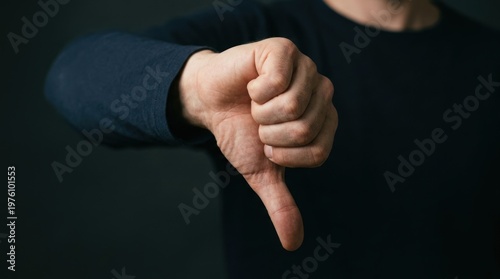 A person is showing a disapproving gesture with their thumb down. The hand is in a dark blue long sleeve shirt.