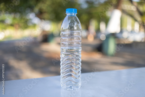 Quadro su tela Clear Plastic Water Bottle on White Table with Blurred Nature Background,A refreshing, full bottle of mineral water stands on a white surface outdoors