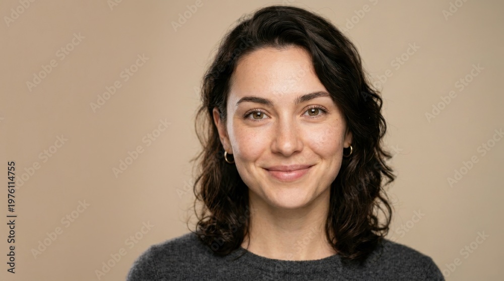Fototapeta premium Portrait of a smiling young woman with dark, wavy hair and warm brown eyes, looking confidently at the camera on a plain background.