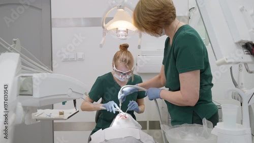 Dentist rinsing teeth with water spray using 3-way syringe while assistant using suction saliva ejector. Professional team removing residue and plaque indicator in stomatology clinic office
