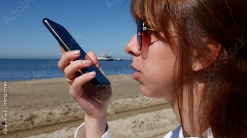 Woman using AI voice assistant on smartphone by the sea.
