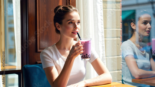 A young woman sips bubble tea while sitting in a cafe. She looks relaxed as sunlight streams through the window. The setting feels lively and warm