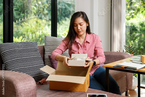 Young female entrepreneur packing a small parcel into a larger cardboard box on a sofa. Online merchant working from home preparing customer orders for shipping.