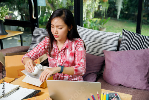 Young Asian female online seller packing a ceramic teapot into a cardboard box with bubble wrap at home. Small business entrepreneur working on e-commerce order fulfillment.