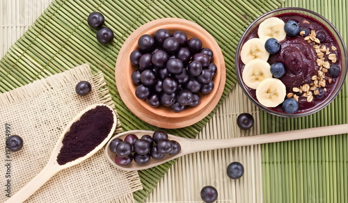 Açaí fruit spread out on a beautiful table along with a bowl of açaí. Next to it, a wooden spoon with açaí powder. Traditional dish from the Amazon region, considered a superfood in Brazilian cuisine.