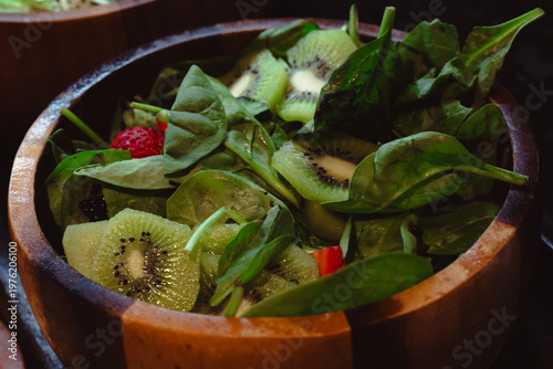 A fresh and vibrant salad made with spinach and kiwi served in a rustic wooden bowl, showcasing healthy eating and a connection to nature through its natural presentation.