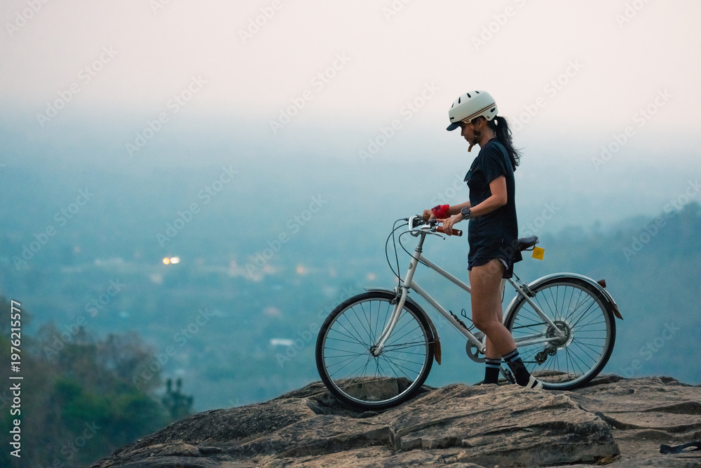 Fototapeta premium Female cyclist mountain bike rocky cliff safety helmet outdoor sport active lifestyle sunset light mountain view adventure travel nature landscape Confident female cyclist with mountain bike rocky