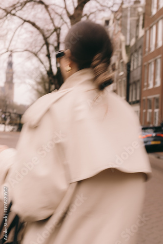 Blurred artistic portrait of a stylish woman in a beige trench coat walking down a European city street with motion blur effect dynamic urban lifestyle cinematic out of focus street fashion aesthetic