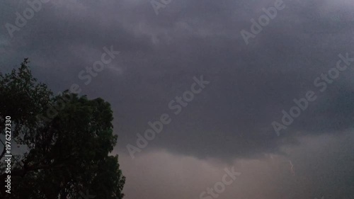 Dark stormy clouds looming above with a silhouette of a tree on the left side creating a dramatic atmosphere