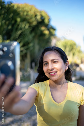 Latin woman enjoying vacation, taking a smiling outdoor selfie with smartphone