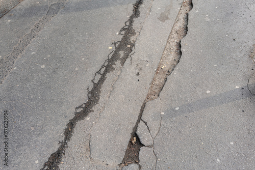 Wallpaper Mural Cracked Asphalt Pavement With Deep Fissures And Small Gravel Debris, Faded Markings And Uneven Surface, Overcast Urban Street Context, Visual Focus On Texture And Decay, Hazard For Vehicles Torontodigital.ca