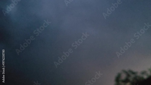 Dramatic sky with dark clouds and a hint of light illuminating the horizon and silhouetted tree branches below