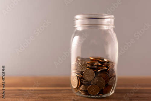 Billede på lærred Glass Jar Half Filled with Pennies on Wooden Surface – Savings Concept Studio Sh