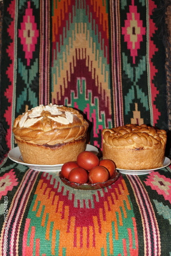 Traditional Easter bread on a colorful geometric kilim rug. Golden braided bread decorated with almonds and red Easter eggs. Festive folk style, warm tones, vibrant colors, appetizing still life.