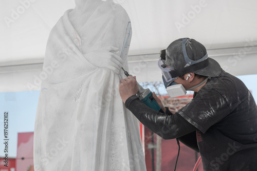 Sculptor carving marble statue in workshop with power tool
