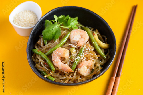 Stir fry noodles with shrimps and green beans in bowl on yellow background
