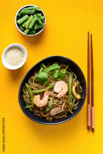 Stir fry noodles with shrimps and green beans in bowl on yellow background
