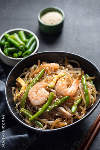 Asian stir fry glass noodles with shrimps and green beans in bowl, black background