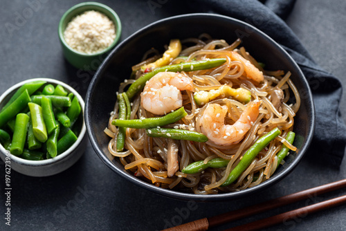 Asian stir fry glass noodles with shrimps and green beans in bowl, black background